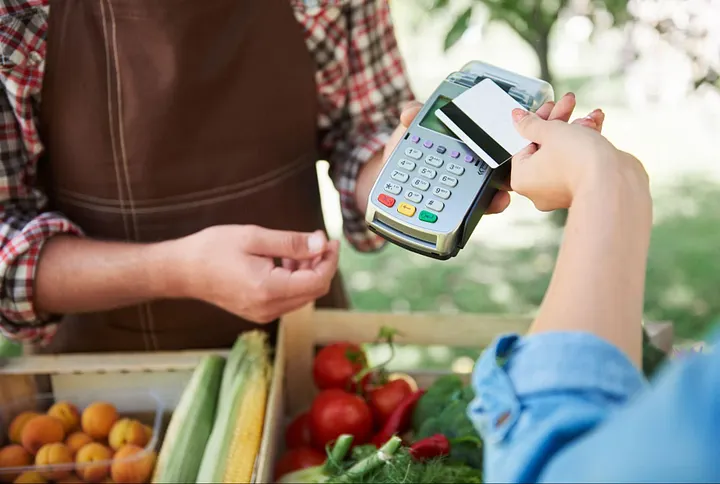 Pazarda mobil POS cihazı ile kartlı ödeme yapan müşteri, hızlı ve güvenli alışveriş deneyimi yaşıyor